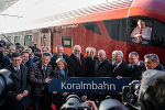 Gruppe von Menschen präsentiert Schild mit Aufschrift "Koralmbahn" vor rotem Zug.