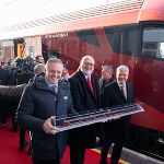 Personen überreichen symbolisch ein Modell eines Zuges. Im Hintergrund ein roter Zug.